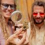 People observing a dried cannabis flower through a magnifying glass during the day