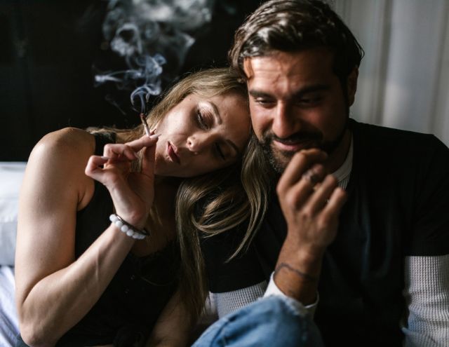 A happy man and woman sharing a cannabis joint in a dark room in the late afternoon.