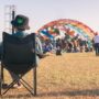 A man in a chair wearing a cannabis bucket hat at a marijuana festival during the day.