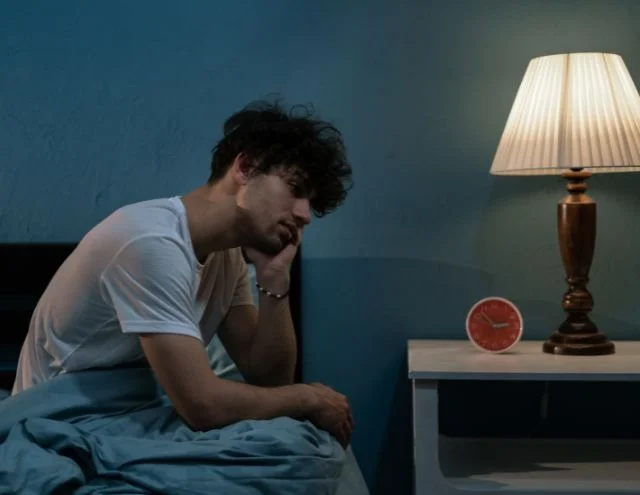 A man in a dimly lit bedroom struggling to get a good night's rest