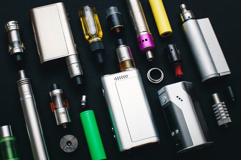 Assortment of vape pens, cartridges, and batteries laid out on a black background.