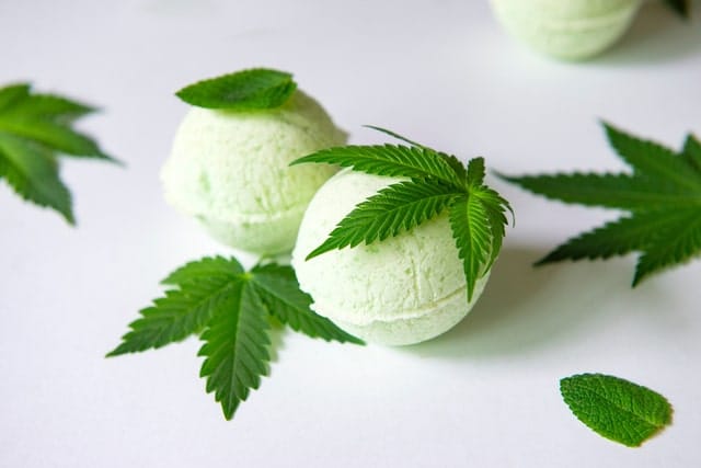 Two light green CBD bath bombs surrounded by hemp leaves, representing the rise of CBD-infused body care products designed for relaxation and skin support.