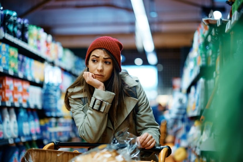 Young woman looking overwhelmed while shopping in a grocery store aisle, representing decision fatigue and stress common among younger adults.