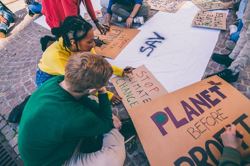Group of young people sitting on the ground creating climate protest signs, illustrating Gen Z’s engagement with environmental anxiety and activism.