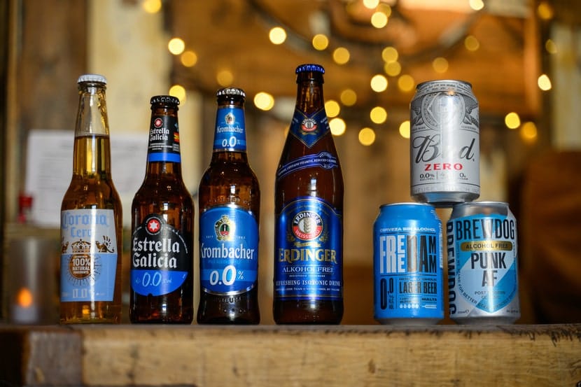 A selection of non-alcoholic beer bottles and cans displayed on a wooden surface with warm lighting in the background.