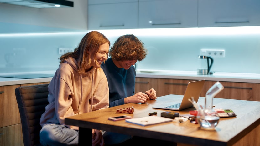 Young adults sitting at a kitchen table with a laptop and cannabis products, showing casual, social cannabis use in a home setting.