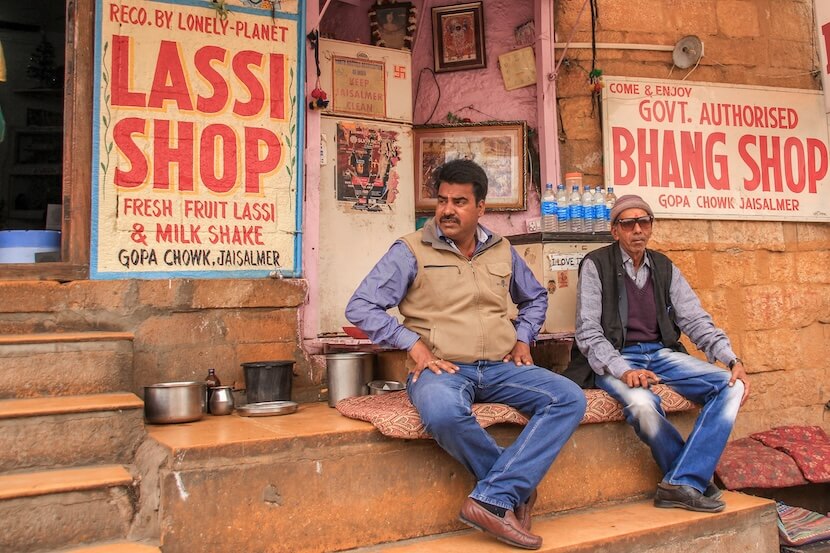 Two Indian men sitting in front of a bhang shop