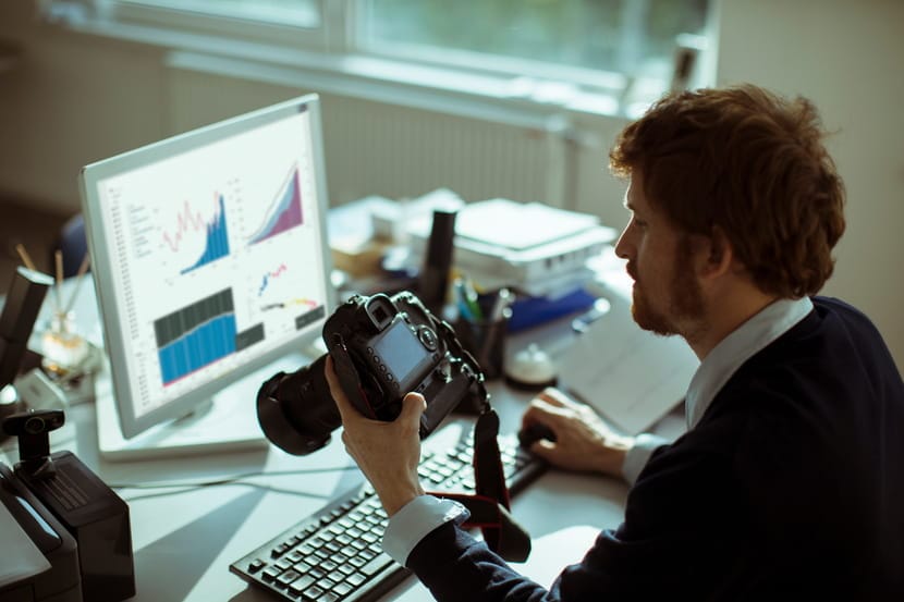 A content creator holds a camera while reviewing performance data on a computer.
